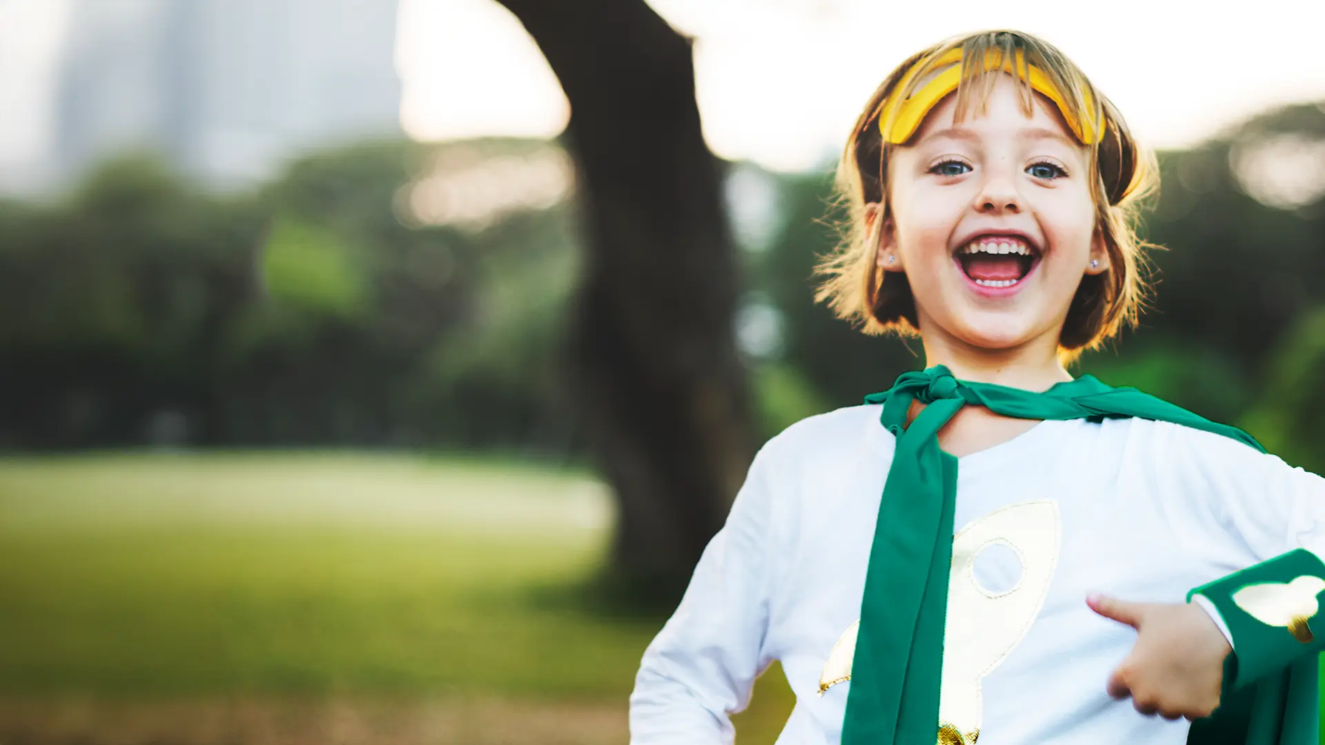 Glad ung flicka med superhjälte kläder på sig i en park.